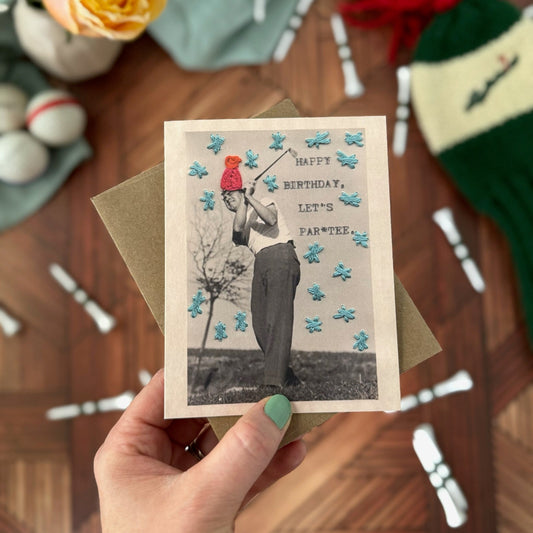 Hand holding a birthday card with a vintage-style photo of a man golfing on a wooden surface with decorative items.