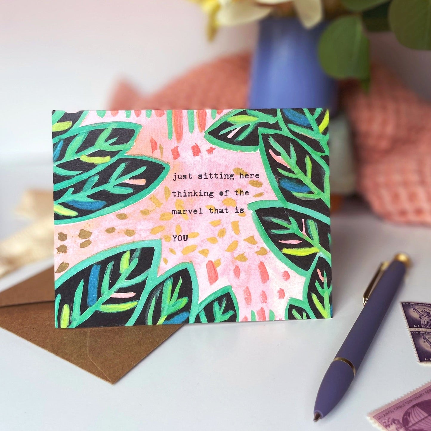 Colorful card with leaf pattern on a table with flowers and stationery items.