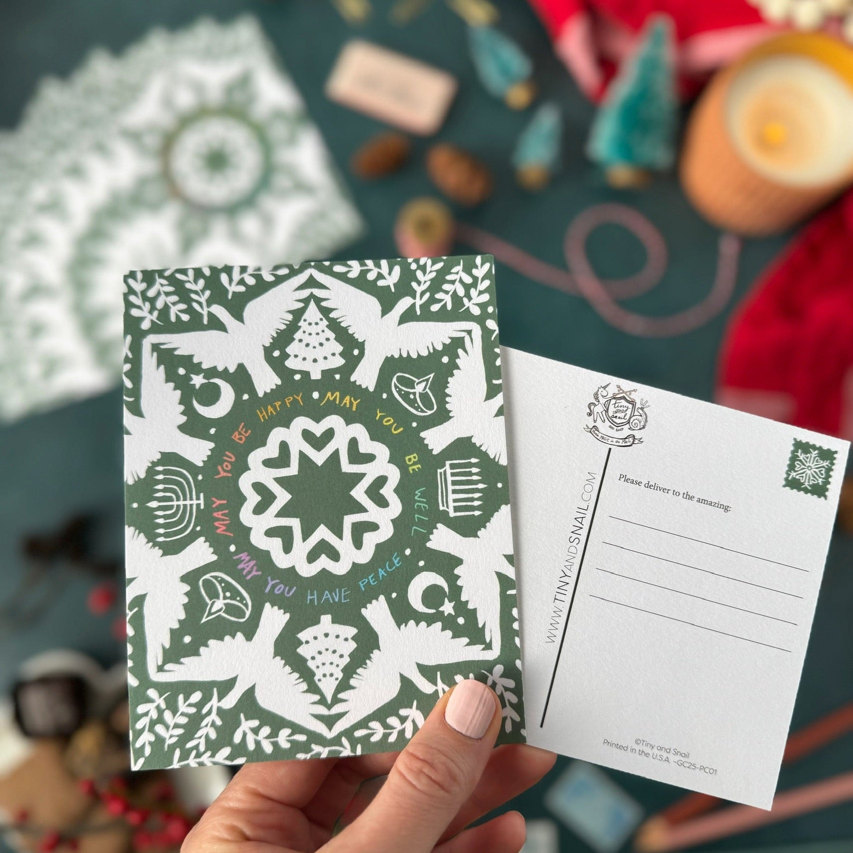 Hand holding a green and white patterned postcard with a festive background