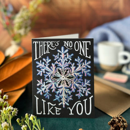 Greeting card with snowflake design and text 'There's no one like you' on a wooden surface.