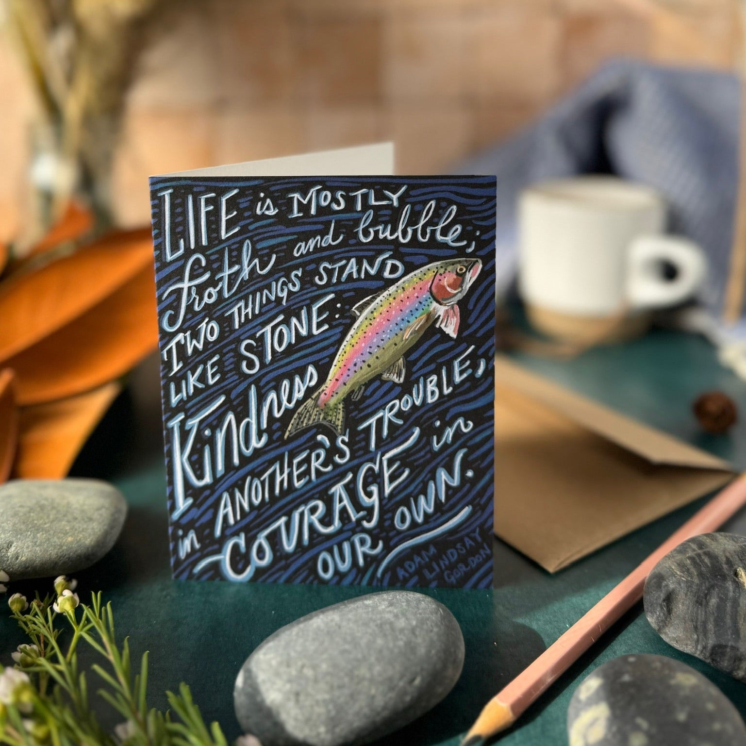 Card with motivational quote on a table with stones and a cup in the background