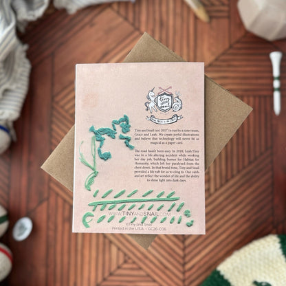 Pink card with green text and graphics on a wooden surface
