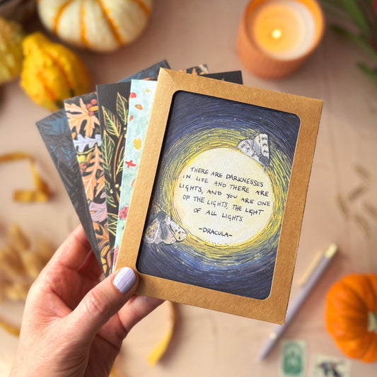 Hand holding a card with a quote surrounded by decorative pumpkins and candles on a wooden surface.