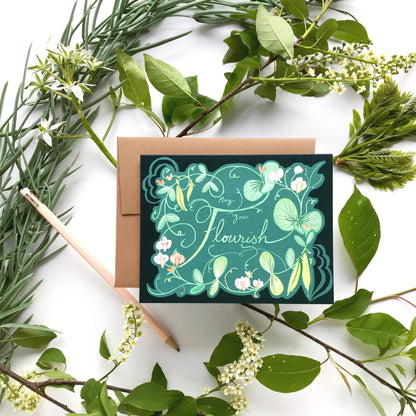 Greeting card that says "May you flourish" with floral design surrounded by greenery on a white background