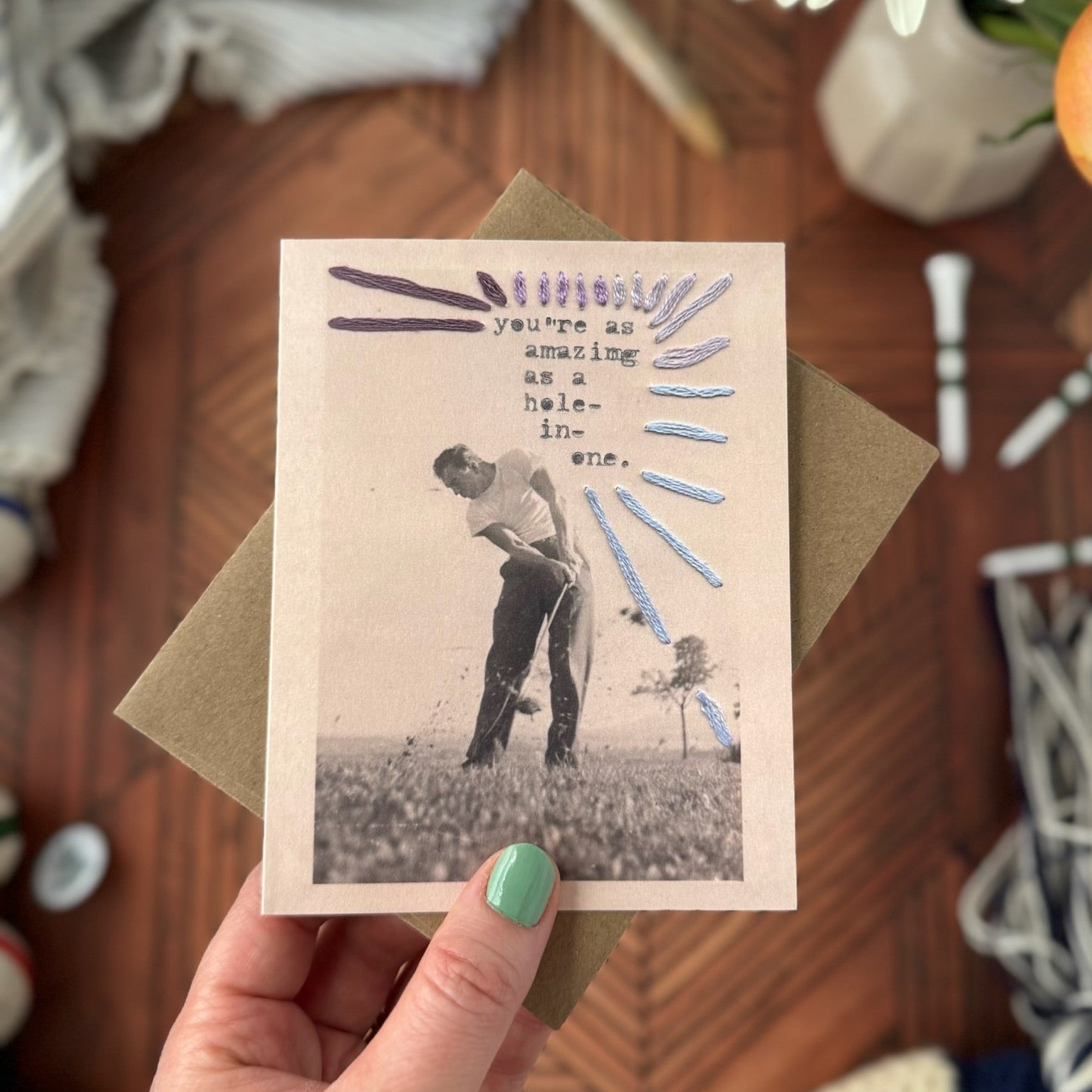 Hand holding a vintage-style greeting card with a golfing scene on a wooden surface.