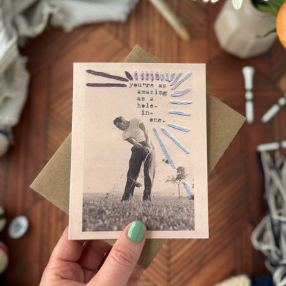Hand holding a vintage-style greeting card with a golfing scene on a wooden surface.