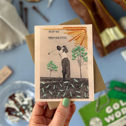 Hand holding a card with a golf-themed design on a table 