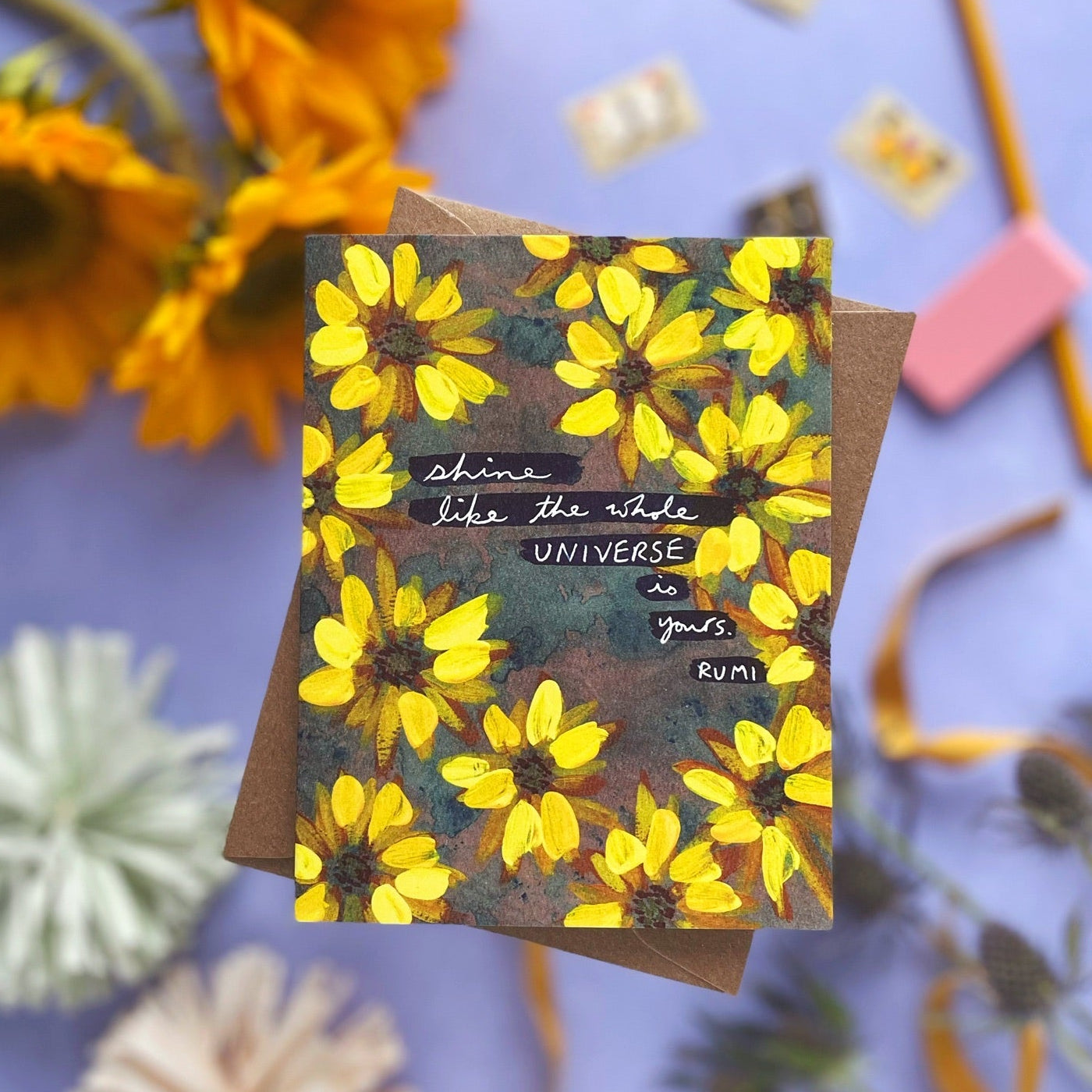 Floral card with sunflower design and motivational quote surrounded by dried flowers on a purple background